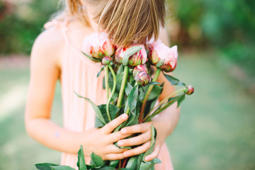 Fototapeta premium Little cute girl holding a bouquet with pink peonies