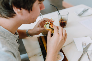 young man in casual clothes eatig a delicious burger in a cafe indoors