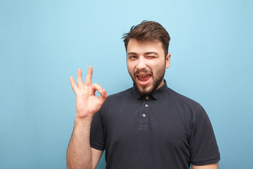 Happy man on a blue background smiles at the sign OK. Bearded man shows what he likes, looks at the camera, isolated on a yellow background. Adult man shows finger symbol OK. Copyspace