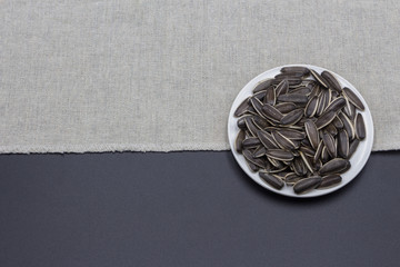 A small plate of black sunflower seeds placed on a blue and white background, a simple food dish...