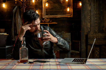 Fototapeta na wymiar Barbershop, shaving. Macho is drinking by his laptop. Thinking. Considering new ideas.