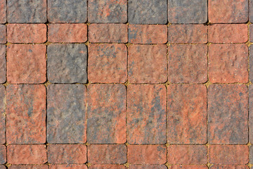 The surface is paved with road tiles of different sizes (multiformat). The uneven (melange) color of the tile makes it look like a natural stone. View from above.