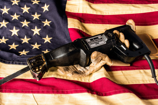 industrial reciprocating saw held by weathered leather work gloves on american flag