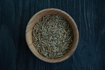 Fototapeta na wymiar Cumin seeds in a wooden dish. Dark wooden background. View from above. Close-up.
