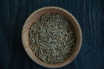Fototapeta na wymiar Cumin seeds in a wooden dish. Dark wooden background. View from above. Close-up.