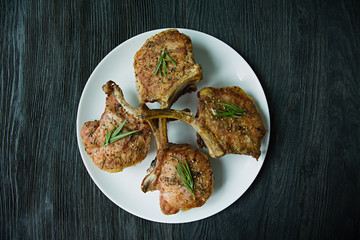 Grilled steaks from pork ribs with spices and herbs. Bone steak. Side view. Dark wooden background.
