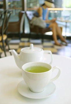 Vertical image of a cup of green tea and teapot on white table in a cafe