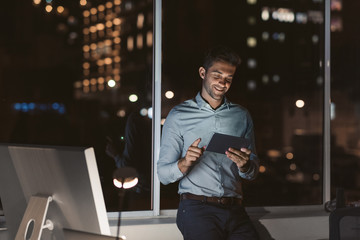 Smiling businessman using a tablet in his office at night