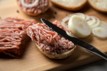 Deutsche Mettbrötchen mit rohen Schweine Mett, Brötchen, Butter, Zwiebeln, Pfeffer und Mett auf Holzbrett mit Messer in Küche