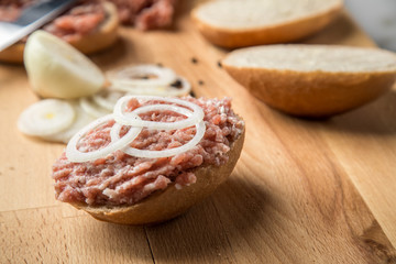Deutsche Mettbrötchen mit rohen Schweine Mett, Brötchen, Butter, Zwiebeln, Pfeffer und Mett auf Holzbrett mit Messer in Küche