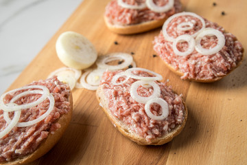 Deutsche Mettbrötchen mit rohen Schweine Mett, Brötchen, Butter, Zwiebeln, Pfeffer und Mett auf Holzbrett mit Messer in Küche