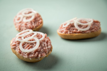 Deutsche Mettbrötchen mit rohen Schweine Mett, Brötchen, Butter, Zwiebeln, Pfeffer und Mett auf Mint Grün Pastell Hintergrund
