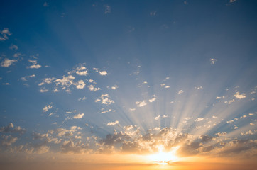 The sun's rays make their way through the clouds at sunset, painting them.