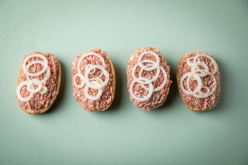 Deutsche Mettbrötchen mit rohen Schweine Mett, Brötchen, Butter, Zwiebeln, Pfeffer und Mett auf Mint Grün Pastell Hintergrund