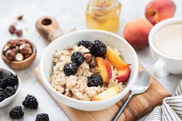 Oatmeal porridge bowl with hazelnuts, peach and blackberry served with cup of coffee. Healthy breakfast, healthy eating, dieting concept