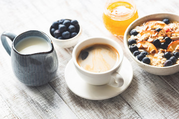 Cup of coffee espresso and breakfast food oatmeal porridge with fruits, berries, honey on rustic white wooden table background