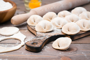 Raw dumplings on the cutting board and ingredients for their preparation on a wooden table