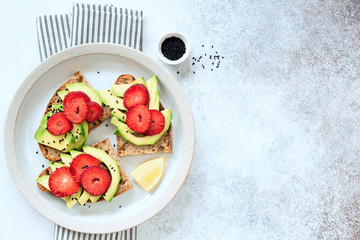 Healthy avocado toast with strawberries on plate, table top view with copy space for text. Tasty vegan food