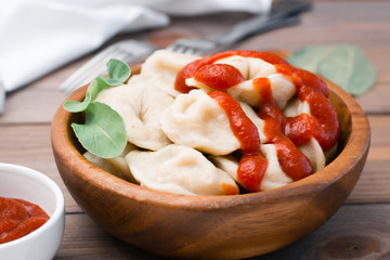 Cooked dumplings poured with ketchup with arugula leaves in a wooden bowl on the table. Close-up