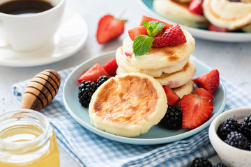 Fried cottage cheese pancakes syrniki served with strawberries, blackberries, honey and cup of coffee. Checkered blue napkin background