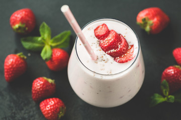 Strawberry milkshake or smoothie in glass with pink drinking straw on black background. Toned image