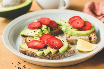 Rye toast with avocado and strawberry on plate. Healthy vegan vegetarian food