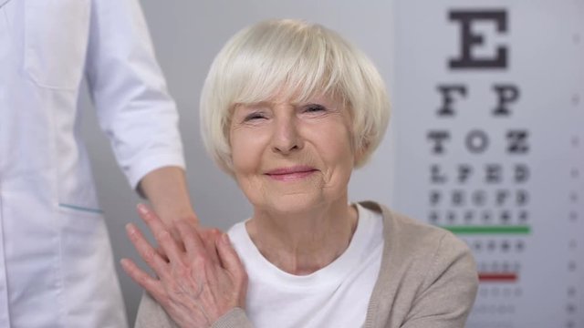 Optician comforting elderly woman squeezing eyes during sight examination, care