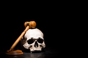 Legal law, justice and murderment concept. Wooden judge gavel hammer on human skull against black...