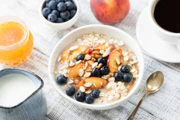 Oatmeal porridge with fruits, honey and cup of coffee on rustic white wooden table. Healthy lifestyle, healthy eating, dieting concept