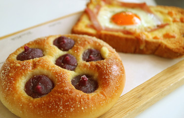 Closeup purple sweet potato cream bun with blurry egg and ham toast in background 