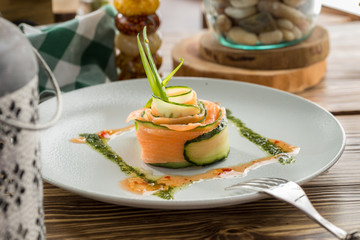 Restaurant Starter with Raw Salted Salmon Slices and Cucumber on white plate on wooden table