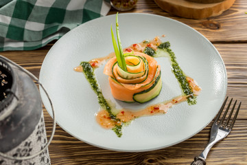 Restaurant Starter with Raw Salted Salmon Slices and Cucumber on white plate on wooden table