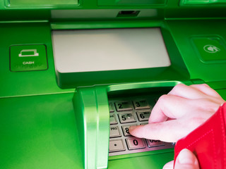 A woman with a red purse in her hands presses a pin code, withdraws money from a green ATM