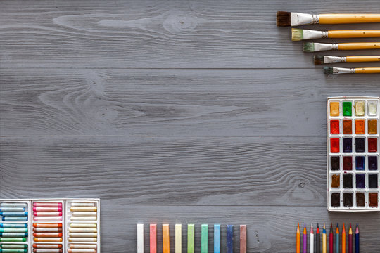 Art Creative Table Background With Watercolor Paints Palette Paintbrushes Pencils Crayons Supplies Tools On Grey Wooden Desk, Artist Gray Design Workspace Top View From Above, Flat Lay, Copy Space