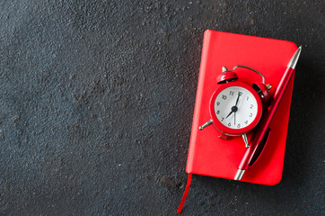 Alarm clock, notepad and pen on dark background. Concept time management or education.