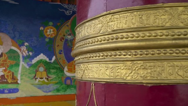 Smooth handheld shot of a spinning buddhist prayer wheel in the Thiksey Monastery in Ladakh, India " Om mani padme hum" written on it. Je Tsongkhapa pictured on the wall.
