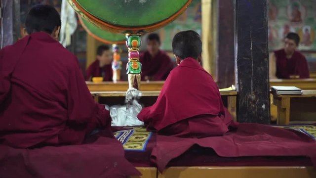Slow motion shot of Buddhist kids, novices sitting in maroon robes on a prayer, shot taken from behind