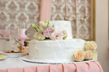 Beautiful two-tiered wedding cake decorated with white cream and rose flowers. Close-up