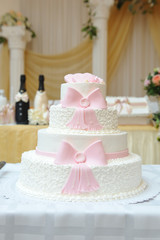 Fototapeta na wymiar A beautiful four-tiered cake decorated with white cream and pink mastic ribbons. Close-up