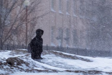 The blizzard, strong wind, sleet, blurred silhouette of the man tries to take cover from bad weather