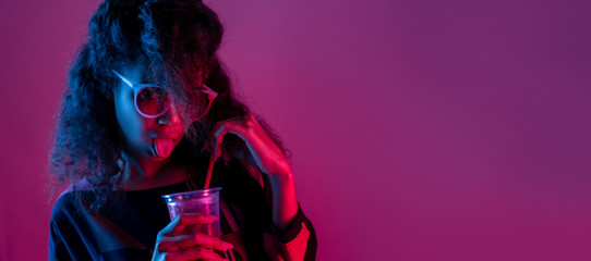Naughty fashion young african girl black woman wear stylish pink glasses hold drink show tongue look at camera isolated on party purple studio background, banner website design, portrait, copy space - obrazy, fototapety, plakaty