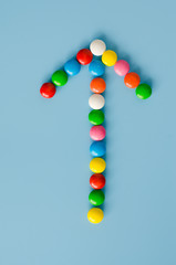 Pointer arrow of chocolate candy with colored glaze on a blue background.