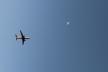 Commercial line flying airplane with rising moon in the background during sunset