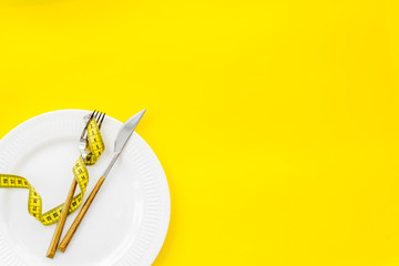Slim concept with plate, flatware and measuring tape on yellow background top view mockup