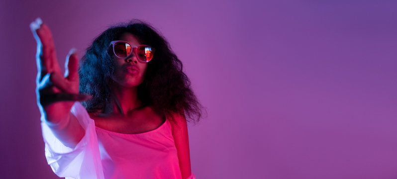 Fashion young african girl black woman wear stylish pink glasses dance look at camera shoot hand gun isolated on party disco purple studio background, banner for website design, portrait, copy space