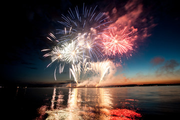 Holiday fireworks above water with reflection on the black sky background