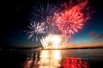 Holiday fireworks above water with reflection on the black sky background