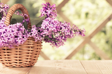Fototapeta premium Basket with a bouquet of lilac flowers on a white wooden table in the summerhouse in the garden