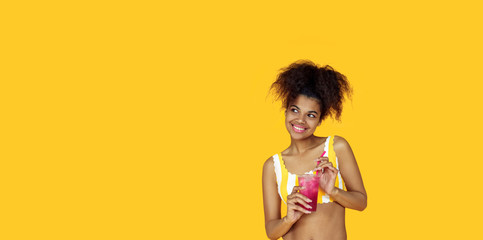 Playful happy young african woman wear stylish yellow clothes holding drink look aside at copy space, black teen girl curious about summer sale isolated on studio background, banner website design