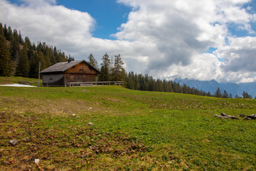 Panorama of an Alpine landscape with high mountains, green meadows, trees and a mountain hut in spring with snow in the Austrian Alps